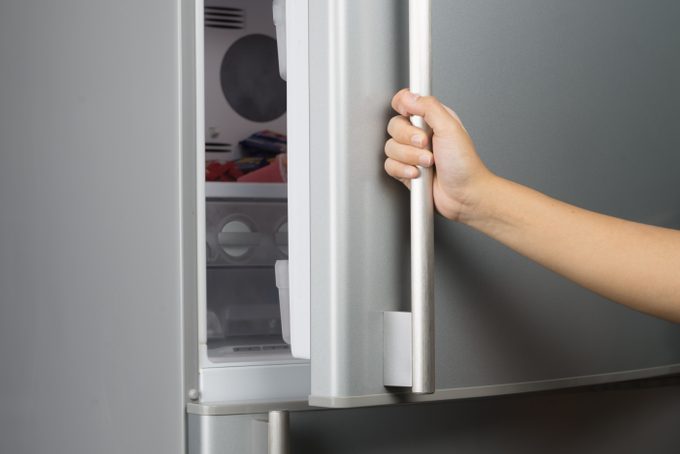Hand of a woman is opening a refrigerator door