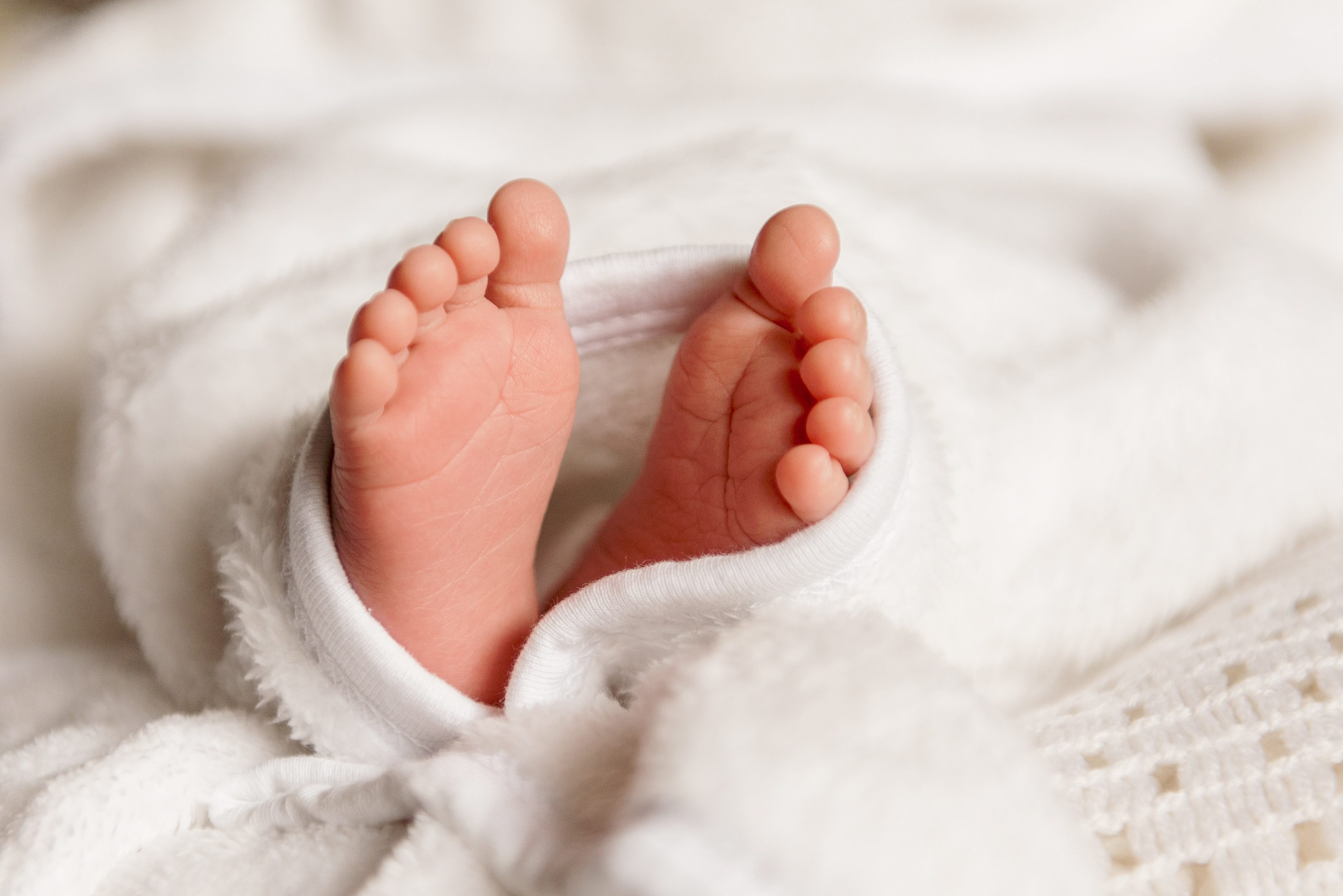 Baby feet resting on soft, white blankets in a cozy setting.