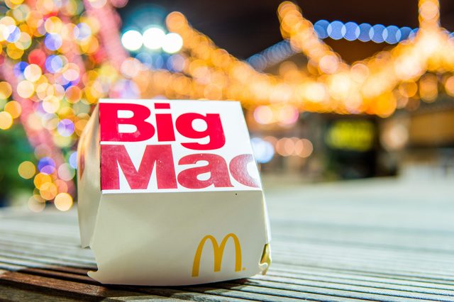 Big Mac box sits on wooden table with blurred, colorful lights in the background.
