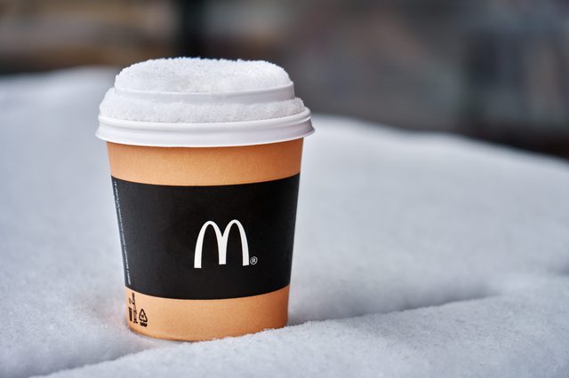 A McDonald's coffee cup sits on snow, covered with a dusting of snowflakes, emphasizing a cold outdoor setting.