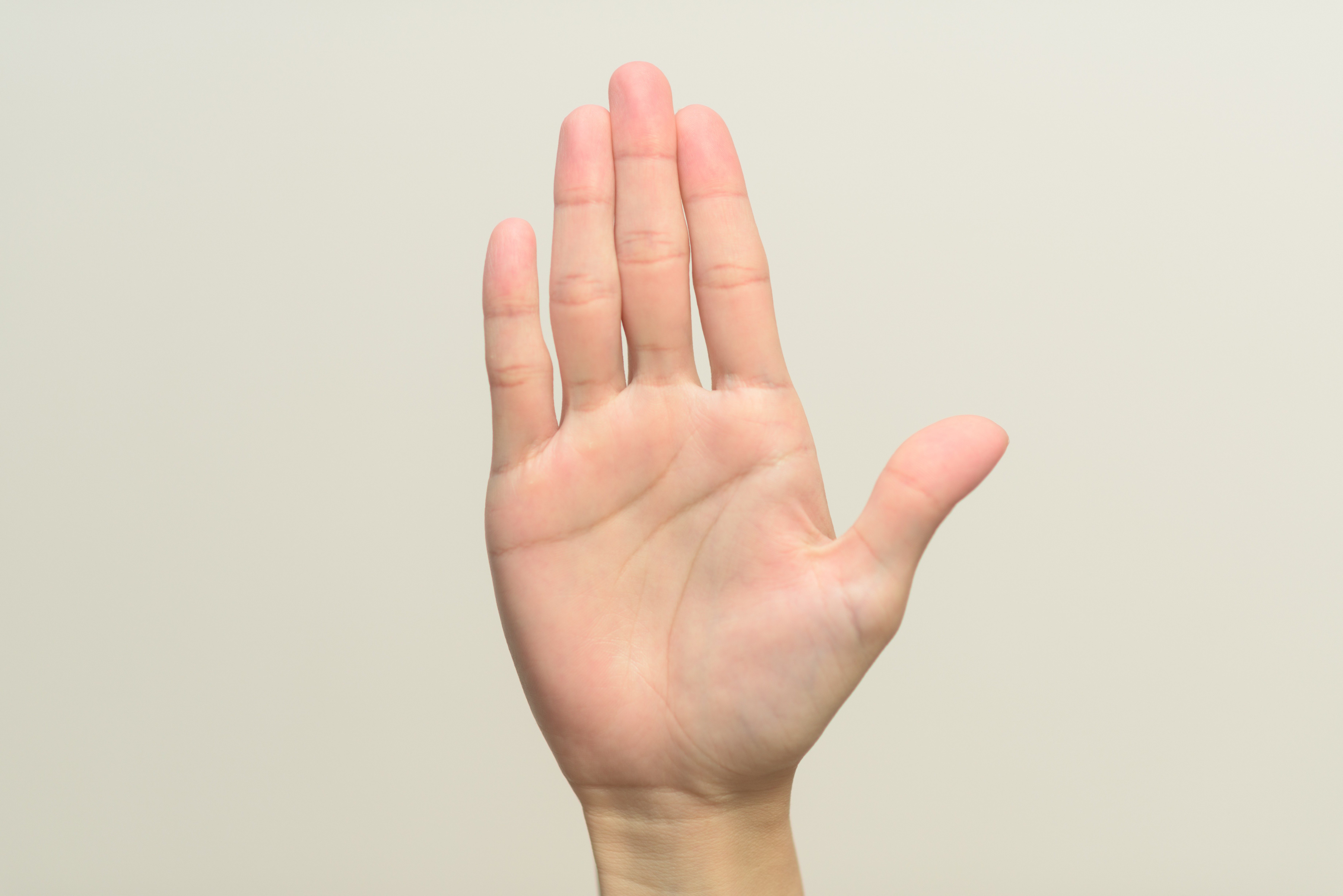 A hand is raised with fingers spread open against a plain beige background.