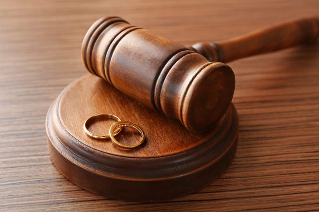 Gavel rests on a wooden block with two gold rings, placed on a wooden table surface.