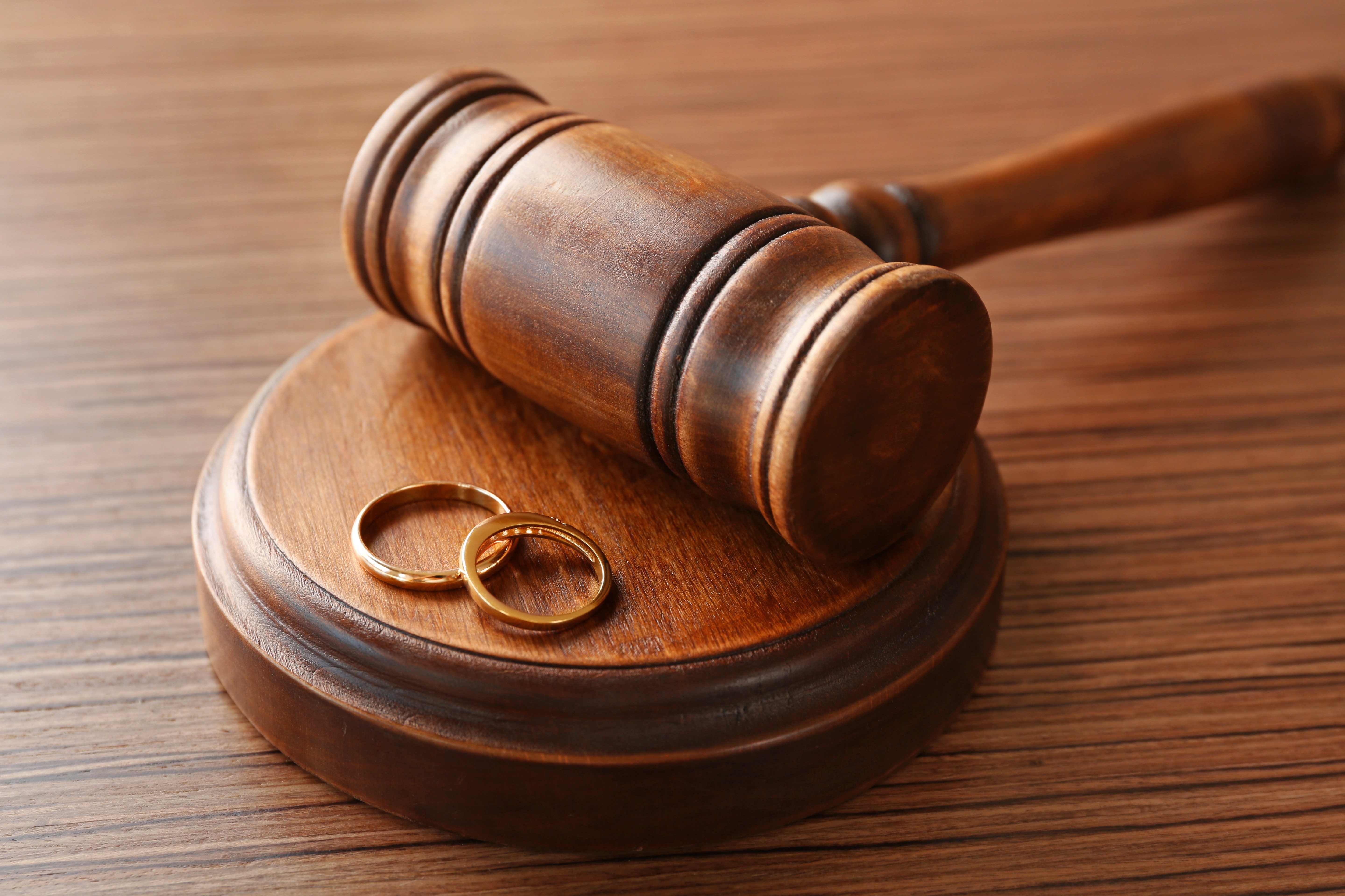 Gavel rests on a wooden block with two gold rings, placed on a wooden table surface.