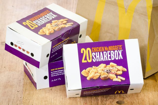 Boxes of "20 Chicken McNuggets Sharebox" sit on a wooden table beside a brown paper bag with a yellow logo.
