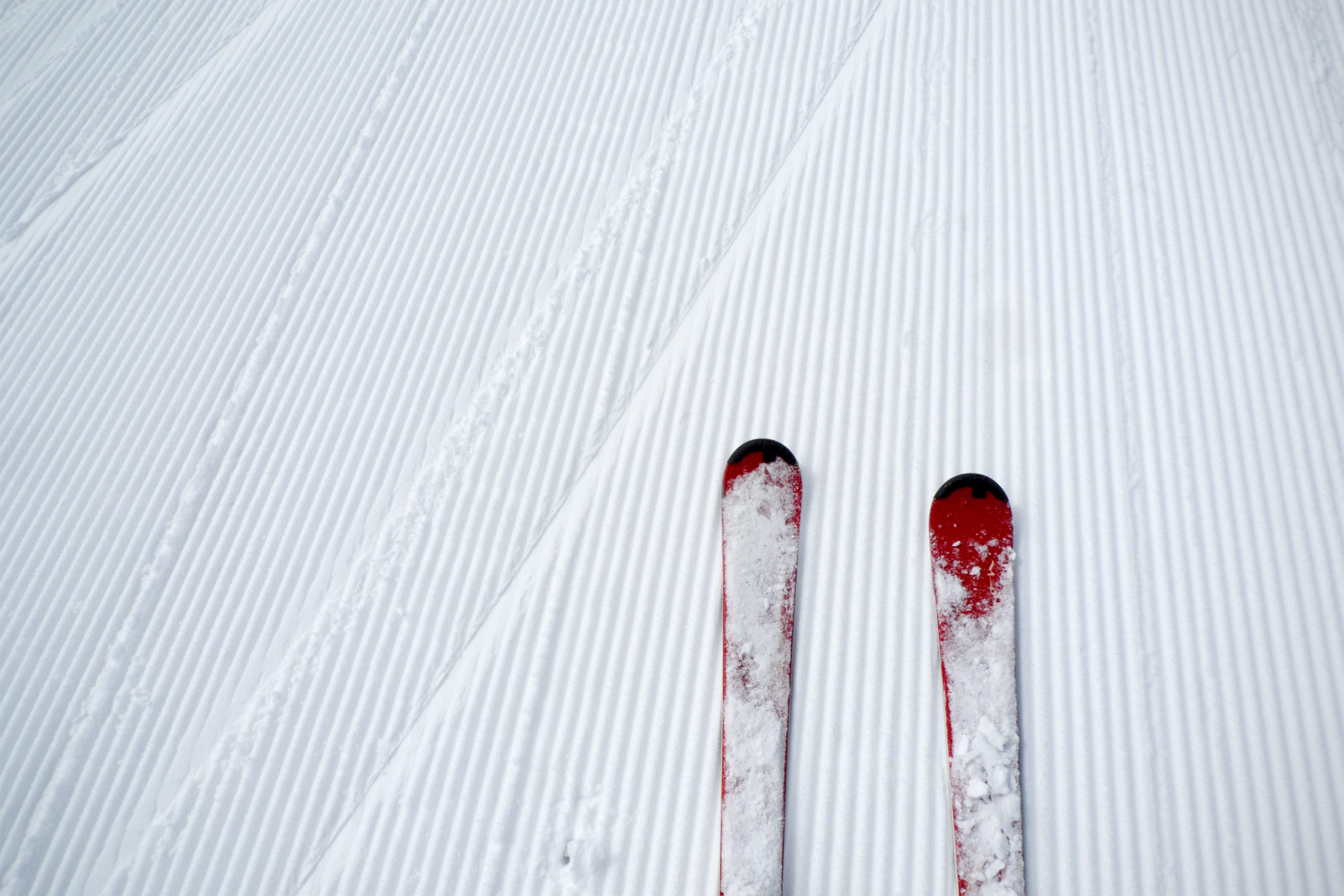 Red skis resting on freshly groomed, parallel grooves of a snow-covered slope, creating a serene winter sports scene.