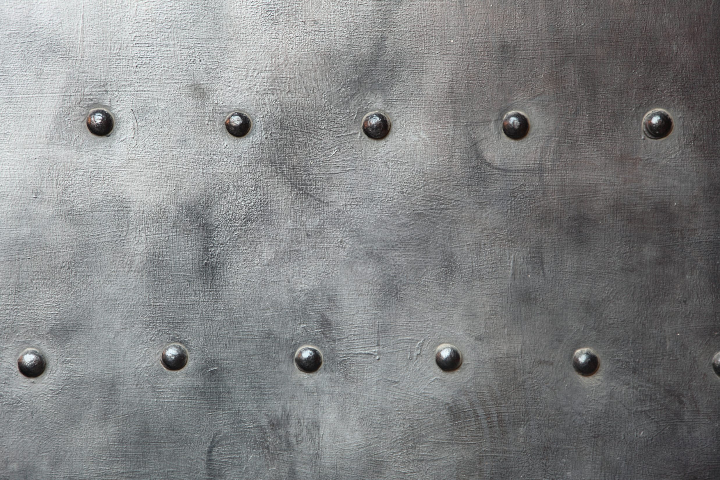 Metal surface with rows of small, round rivets, showing a textured, slightly weathered appearance.