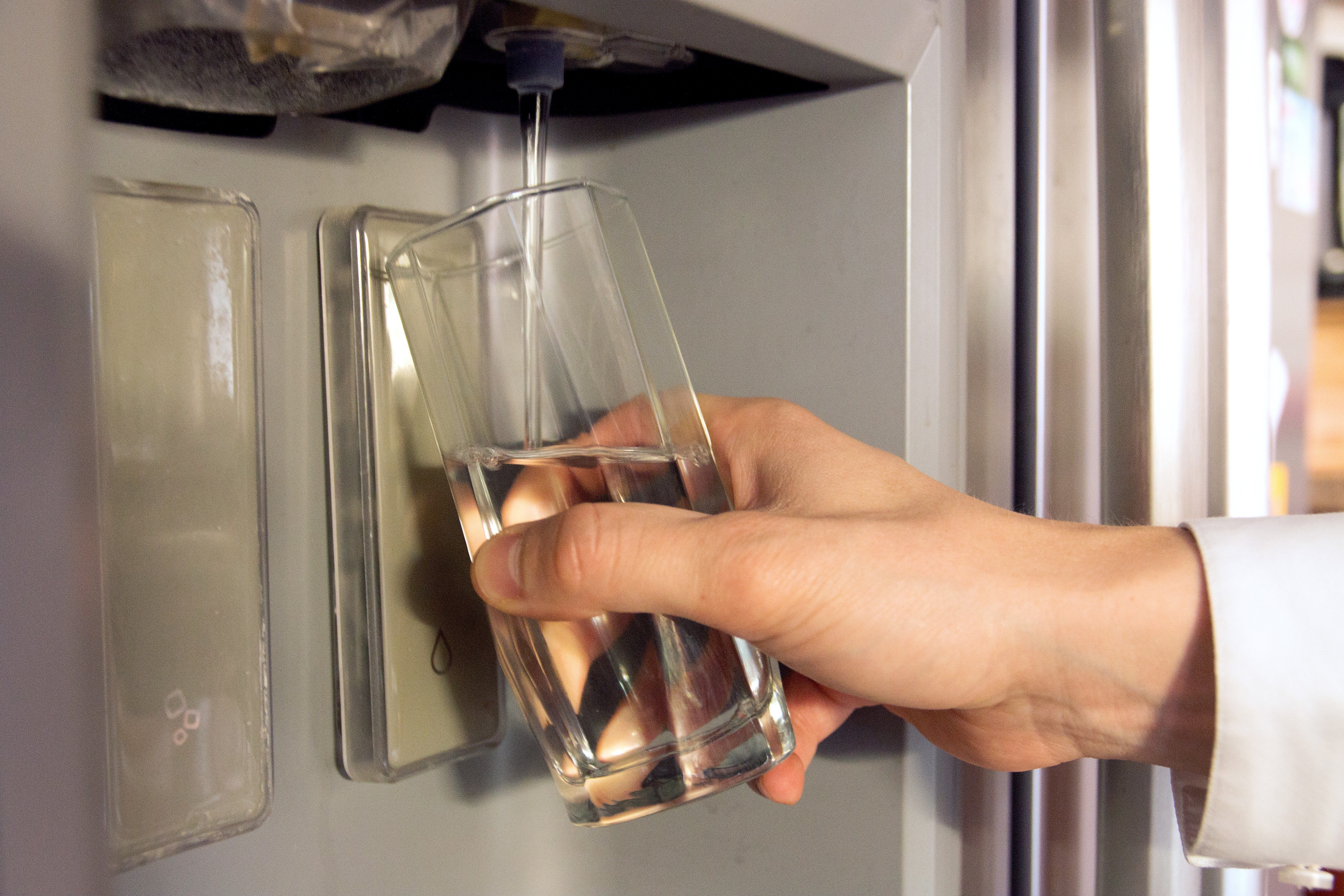 Hand holds a glass; water fills it from a refrigerator dispenser.