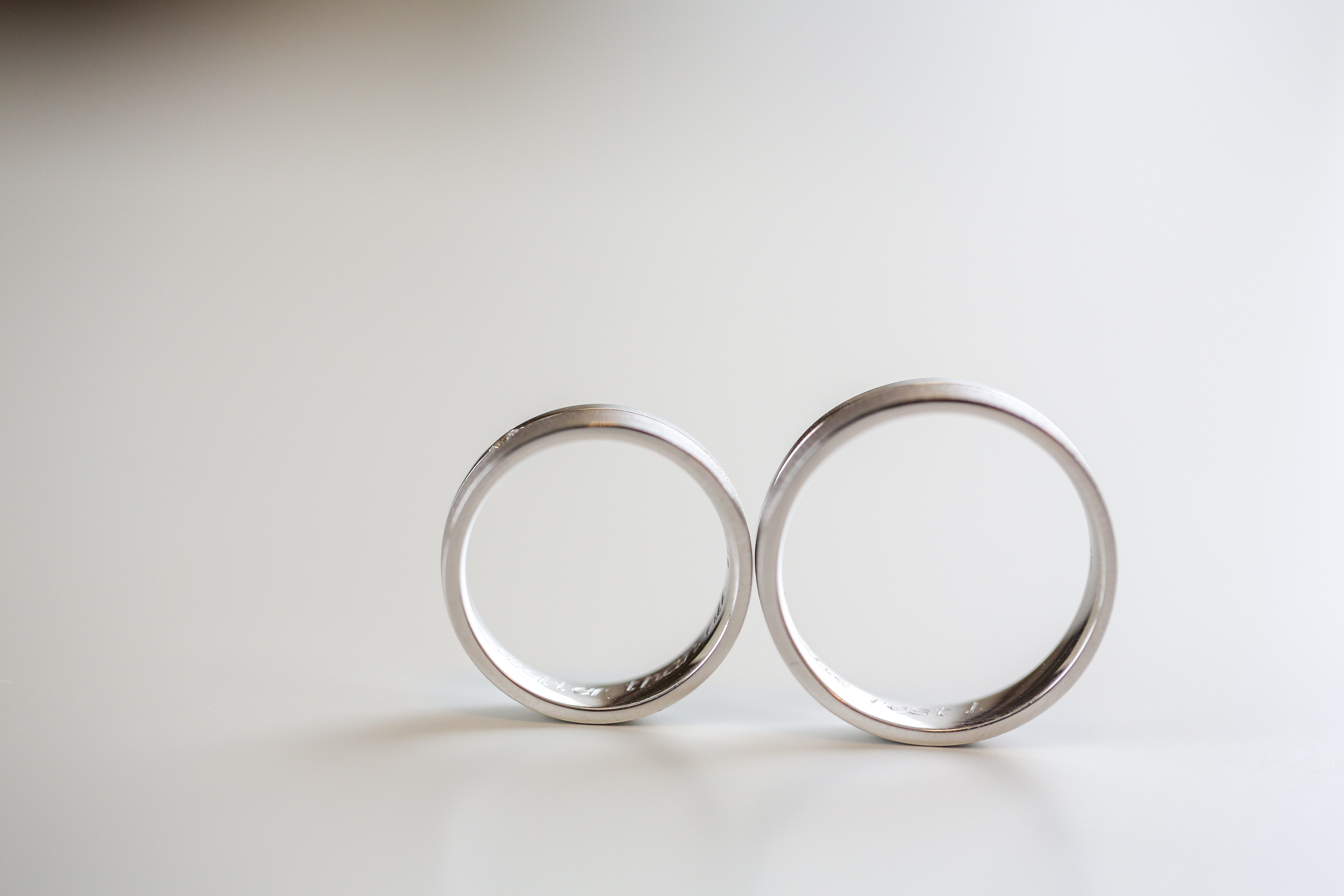 Two silver rings stand upright on a smooth, light surface, casting faint shadows in soft lighting.