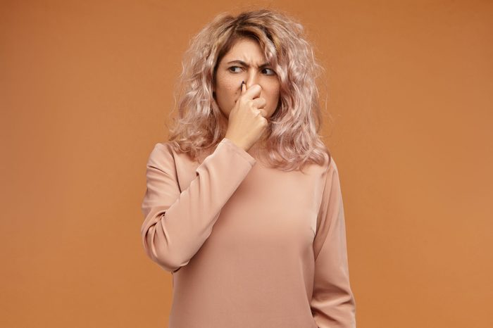 Picture of emotional displeased young European woman pinching her nose because of bad smell or gross stink. Stylish teenage girl can't stand dirty socks odour, holding breath. Body language