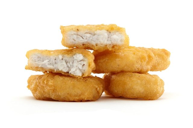 Golden-brown chicken nuggets stacked, one halved to reveal white meat, against a plain white background.