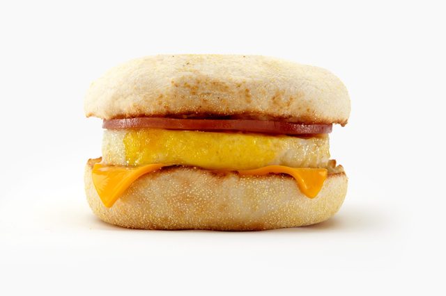 Breakfast sandwich sits on a white surface, featuring an English muffin, egg, cheese, and sausage patty, layered neatly.