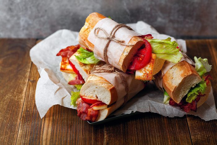 Fresh baguette sandwiches bahn-mi styled with bacon, roasted cheese, tomatoes and lettuce on wooden background