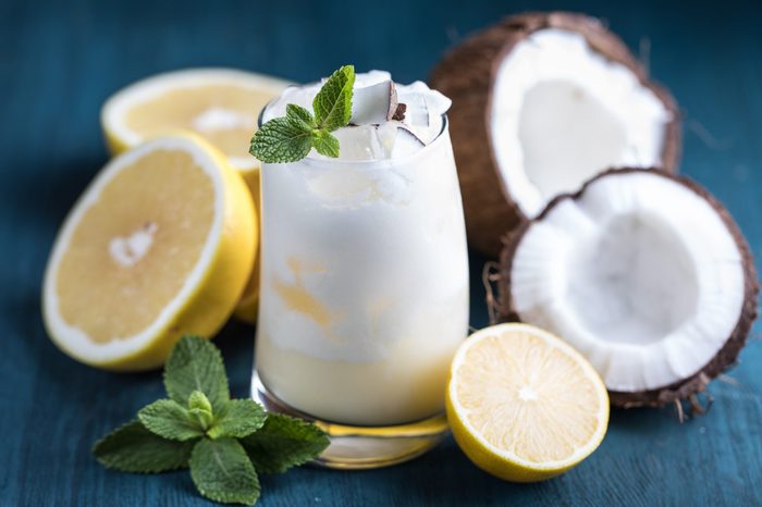 Fresh summer detox cocktail with pineapple juice, coconut milk, white grapefruit, lemon and mint in the glass on the blue wooden background