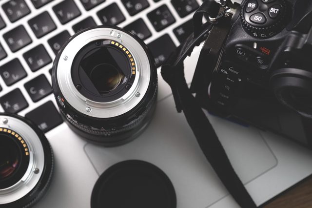 Camera lenses resting on a laptop keyboard, with a digital camera nearby, creating a photography workspace setting.