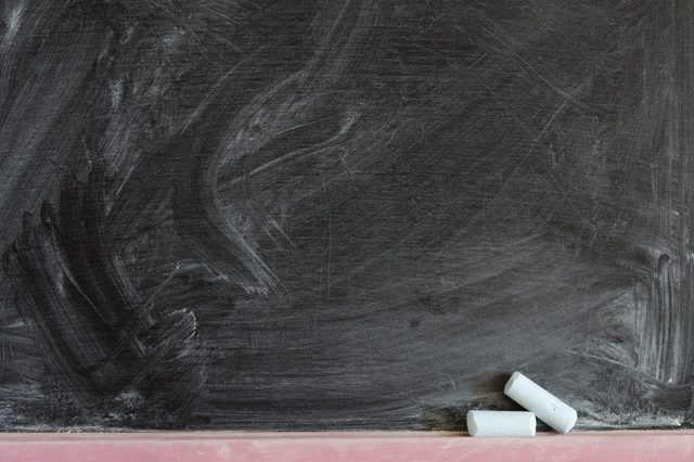 Chalk rests on a blackboard with smudged white marks in a classroom setting.