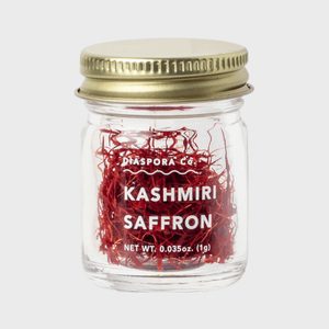A glass jar contains red saffron threads. The lid is metallic gold. Text reads: 