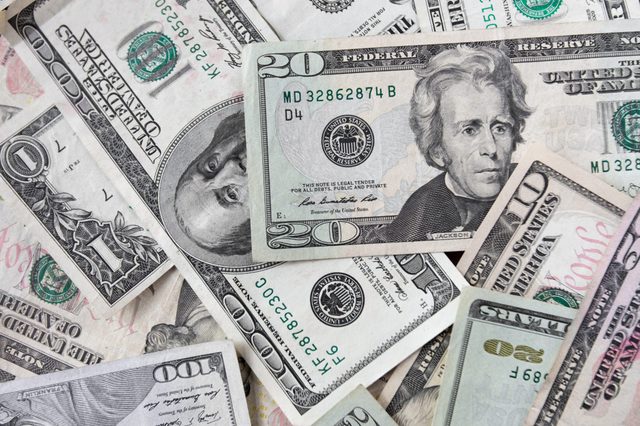 US dollar bills scattered, displaying different denominations, including $10, $20, $50, and $100, featuring presidential portraits in a random arrangement.