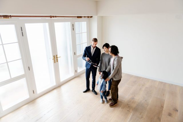 Agent shows paperwork to family in empty room with wooden floor and large frosted glass doors.