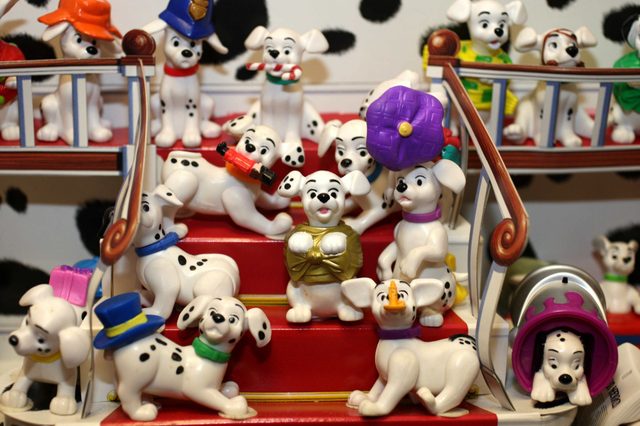 Dalmatian figurines sit playfully on red stairs, wearing accessories like hats and scarves, surrounded by a backdrop with black and white spots.