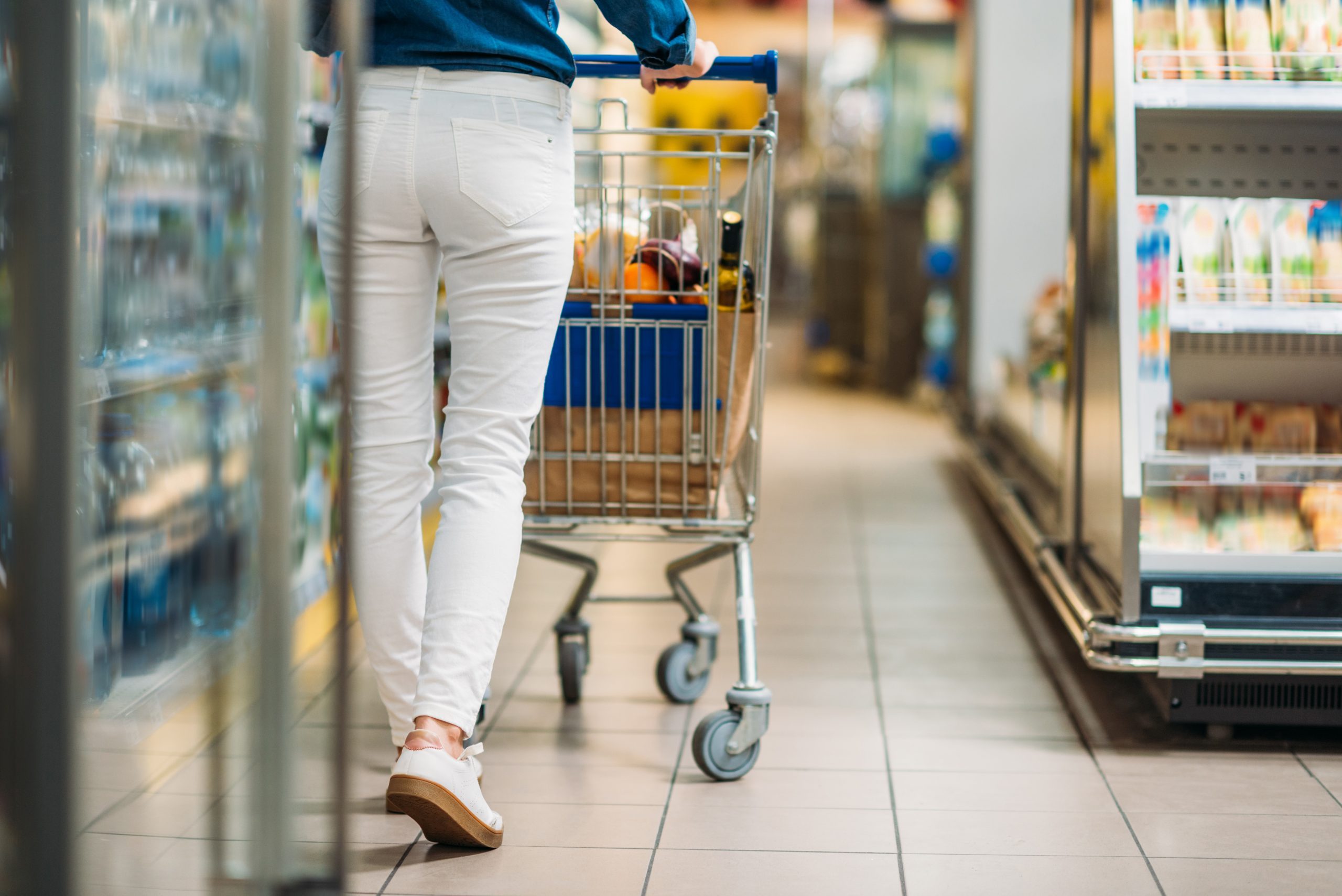 cropped shot of woman with shopping cart walking in supermarket