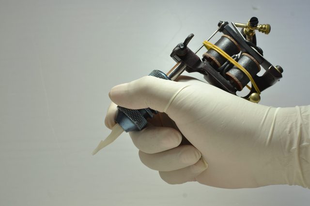 Tattoo machine held by a gloved hand, poised for use against a plain, light background.