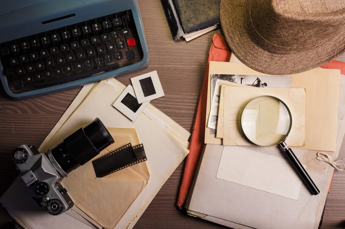 Investigator desk with confidential documents, camera, magnifying glass, vintage typewriter and hat. Secret documents investigation concept.