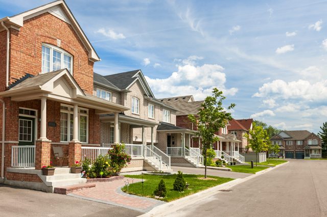 Townhouses line a suburban street, showcasing landscaped front yards with porches under a bright blue sky.