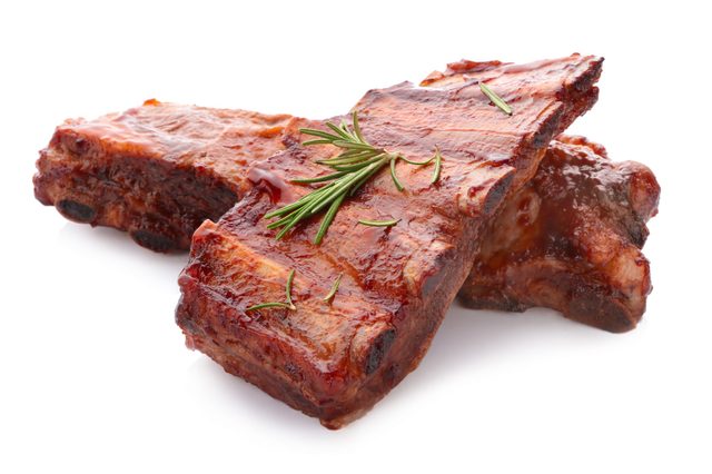 Barbecued ribs lying on a white surface, glistening with sauce, garnished with fresh rosemary sprigs.