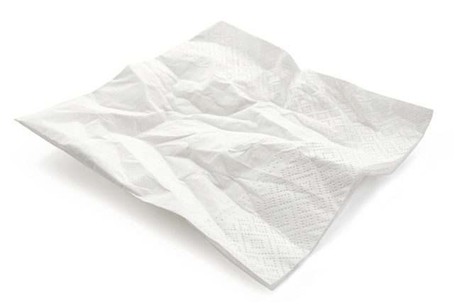 Wrinkled white paper napkin, laying flat on a bright surface, showing embossed patterns and creases.