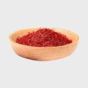 A wooden bowl holds a pile of vibrant red saffron threads on a plain white background.