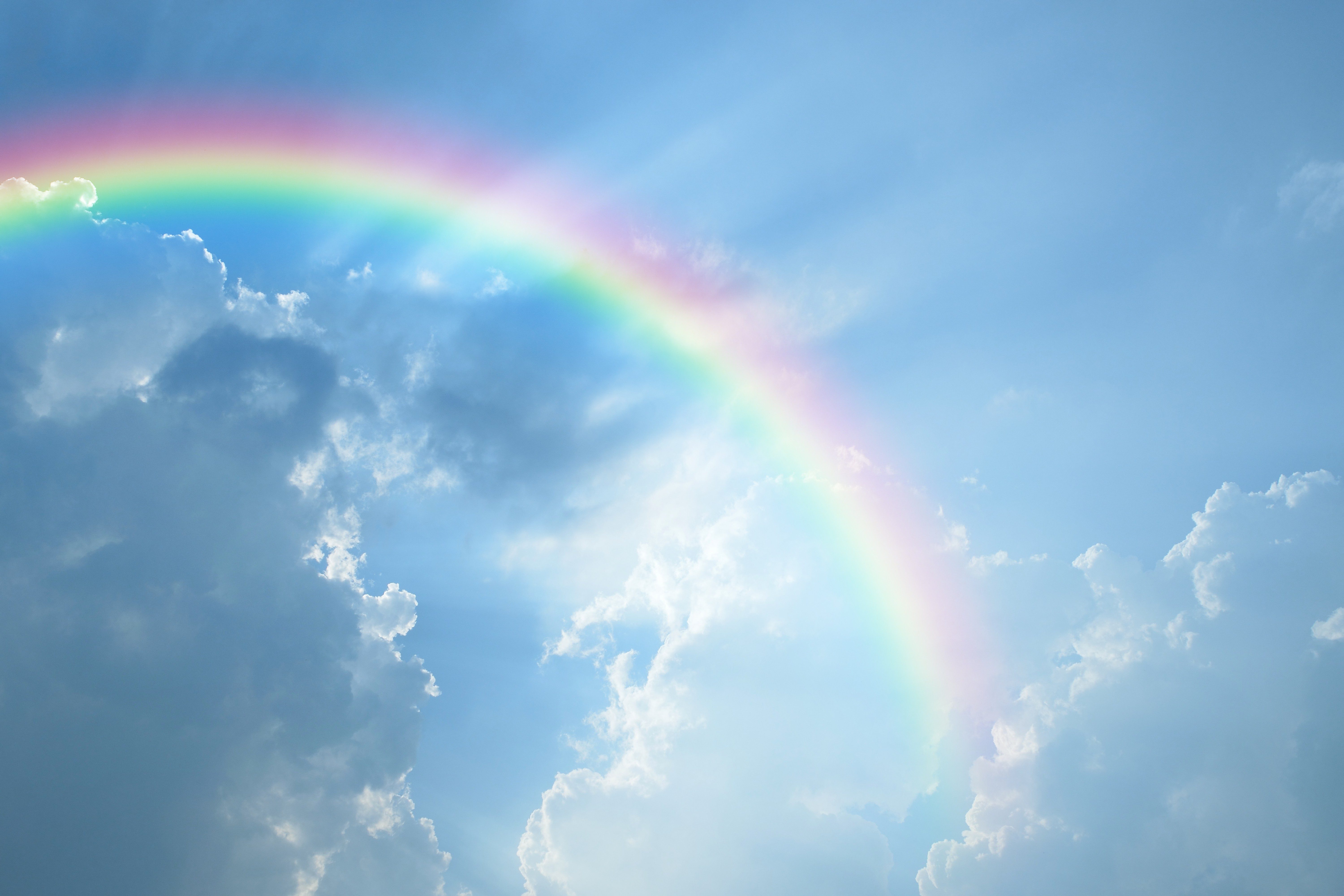 Rainbow arcs across a blue sky among fluffy clouds, creating a serene atmosphere.
