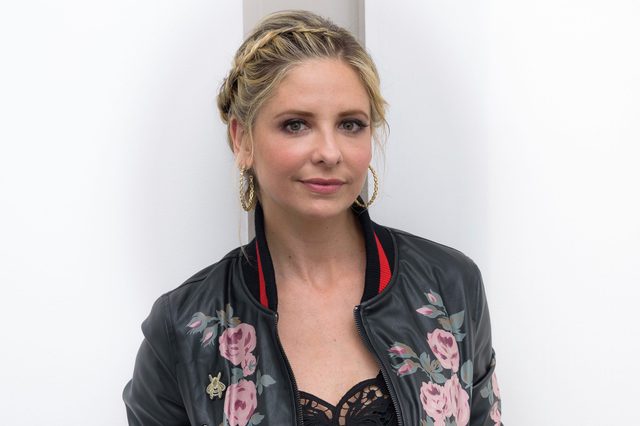 Person standing, wearing a floral leather jacket and hoop earrings, against a plain white background.