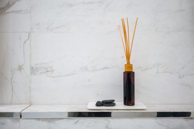 Reed diffuser with black stones sits on a white tray against a marbled wall, creating a minimalist, elegant setting.