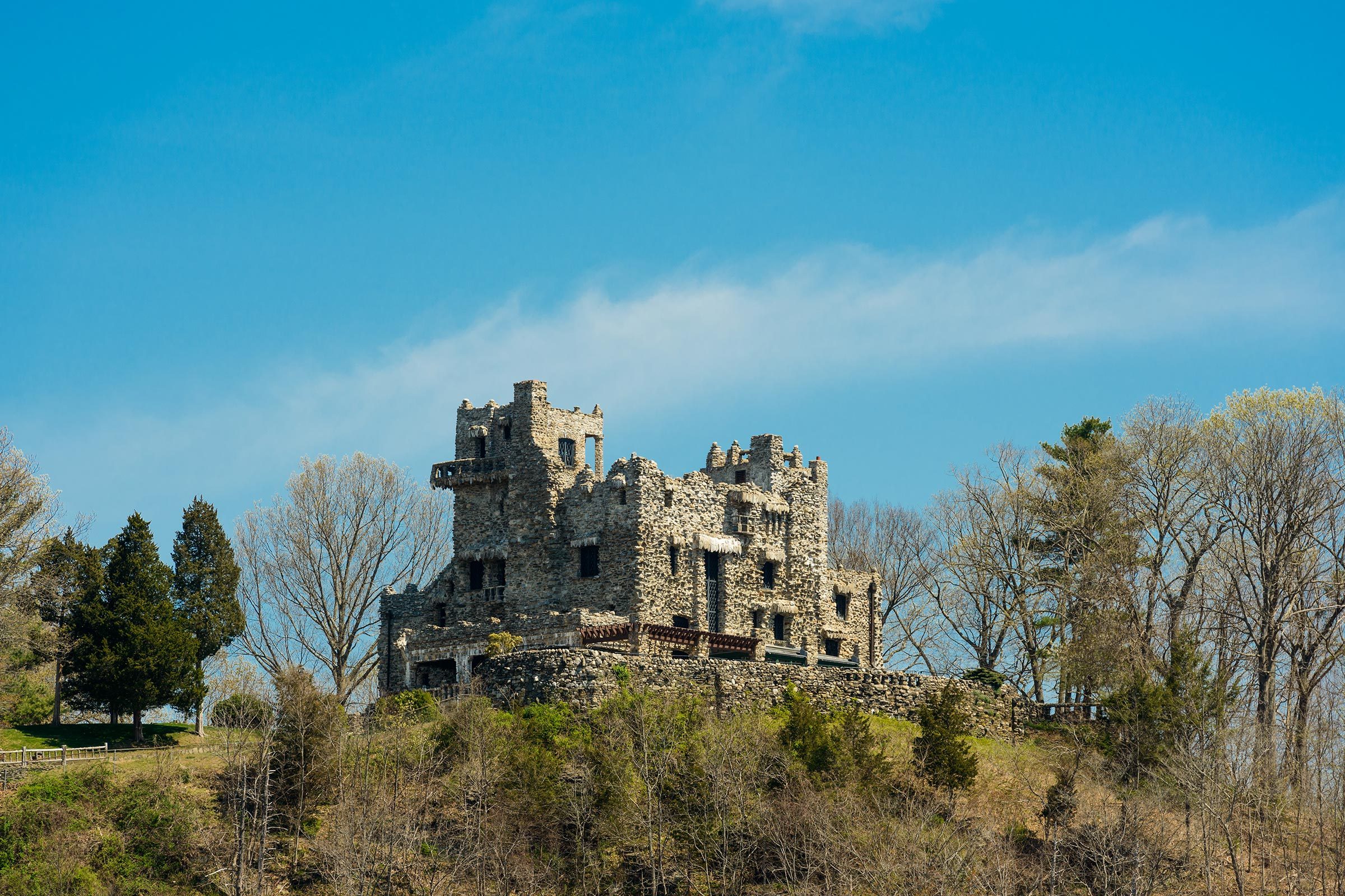 A stone castle sits atop a grassy hill, surrounded by sparse trees under a clear blue sky.