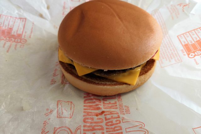A cheeseburger rests on logo-printed wrapping paper, with melted cheese visible inside.