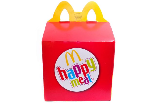 Red Happy Meal box with yellow handles, featuring a colorful logo, situated against a white background.