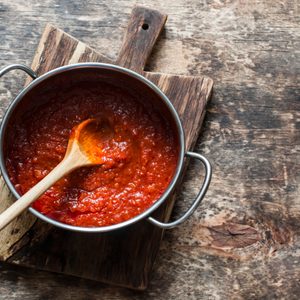 A pot of tomato sauce is stirred with a wooden spoon on a rustic wooden table.