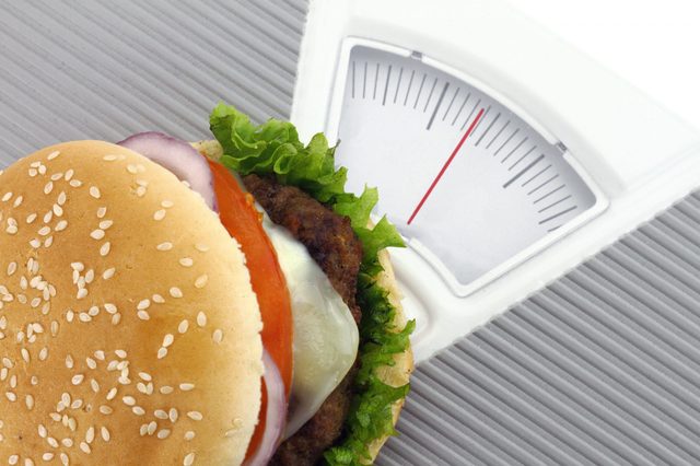 Burger rests atop a scale, showing weight, surrounded by a textured gray surface.