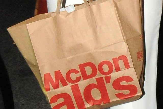 Brown paper bag with "McDonald's" in red, carried by someone in a dim setting.