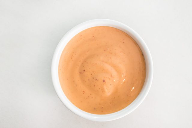 A small bowl holds light orange creamy sauce, displaying a smooth texture, against a plain white background.
