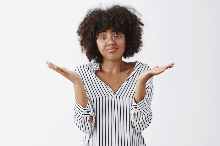 Waist-up shot of upset woman losing in battle shrugging with spread palms aside pursing lips and frowning from disappointment and regret being unhappy and gloomy after bad result over gray wall