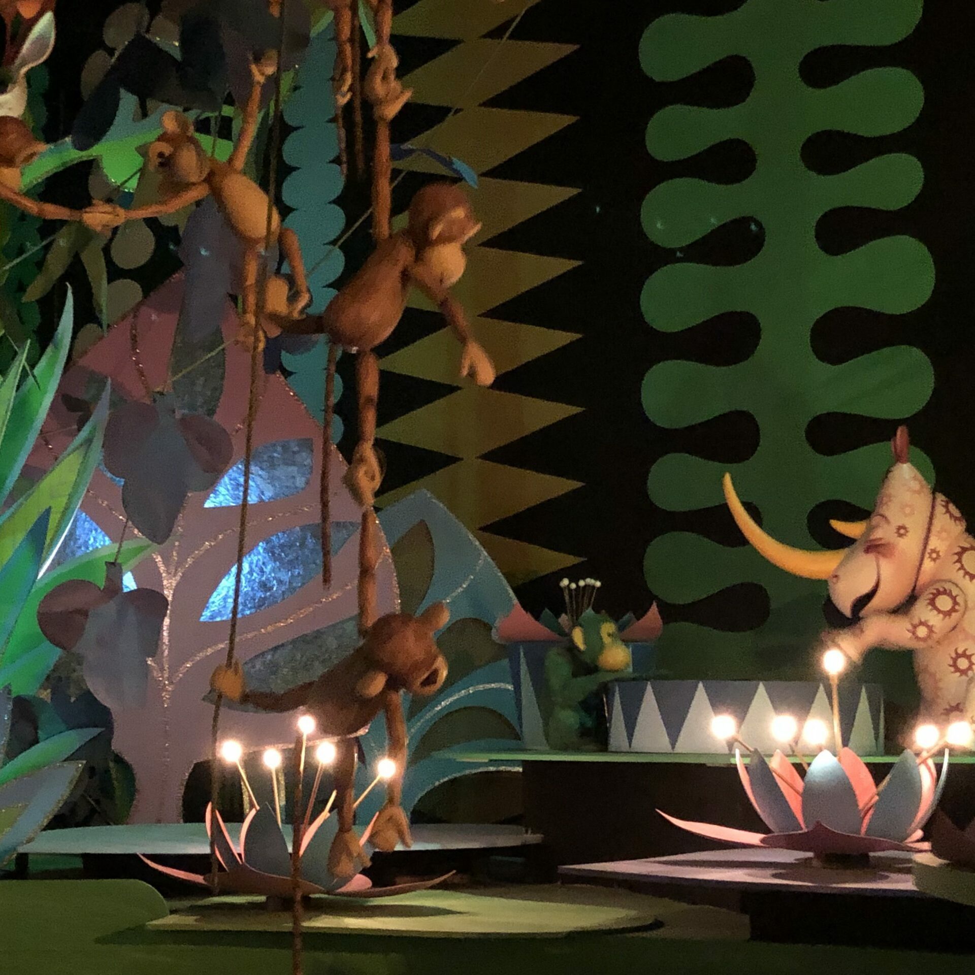 Monkeys hang on vines above lotus-shaped lights, surrounded by colorful plants and a patterned rhino in a whimsical jungle scene.