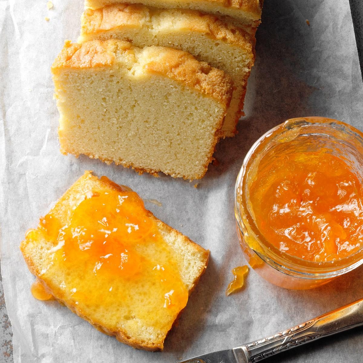 Sliced loaf with marmalade spread, next to a jar of orange jam on parchment paper.