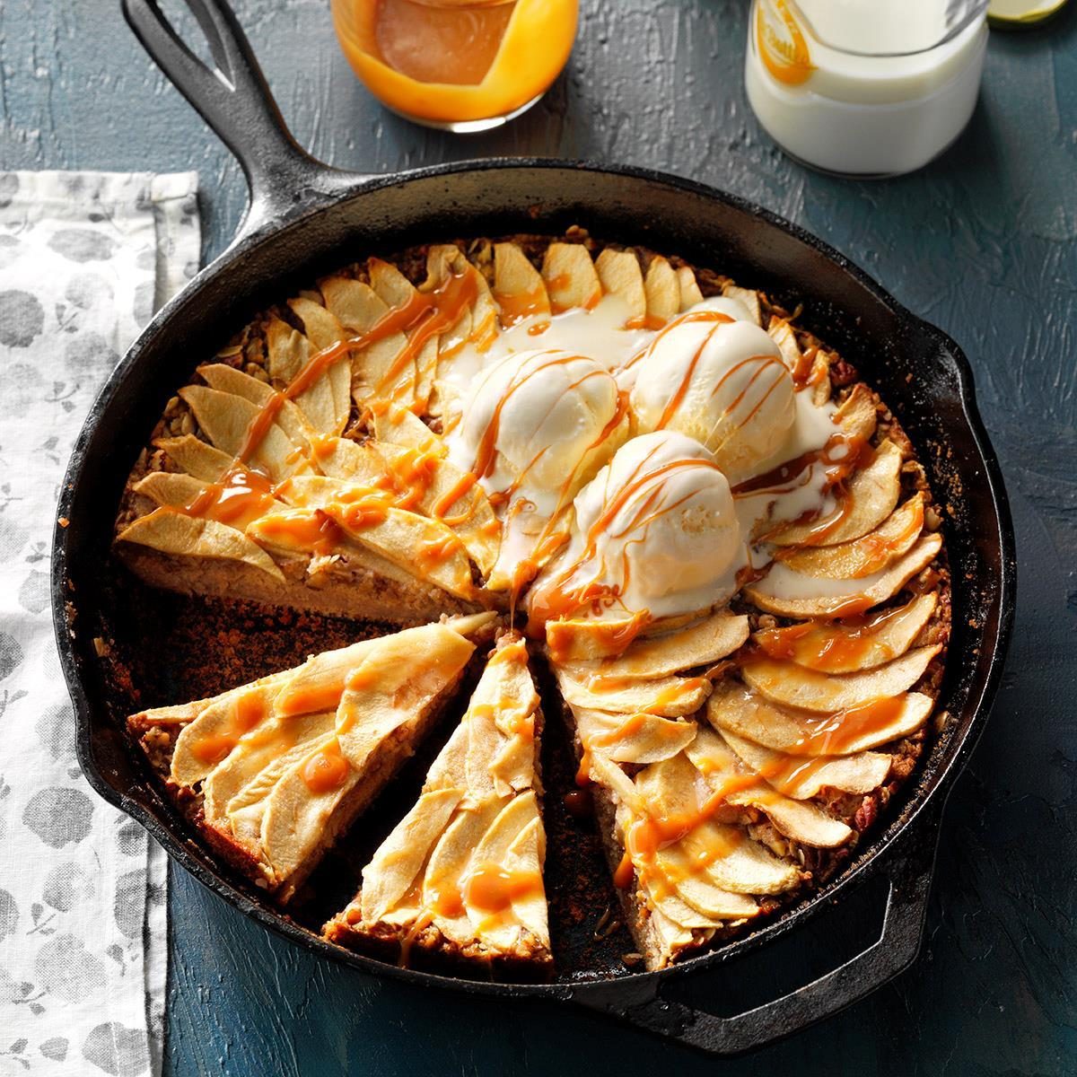Skillet pie topped with caramel drizzled ice cream, served on a dark table with a milk glass and caramel jar nearby.