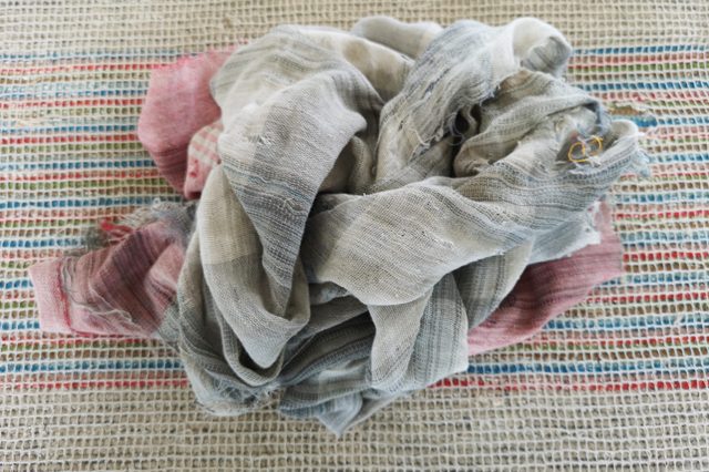 A crumpled, multicolored fabric rests on a woven, striped textile background displaying red, blue, and green lines.