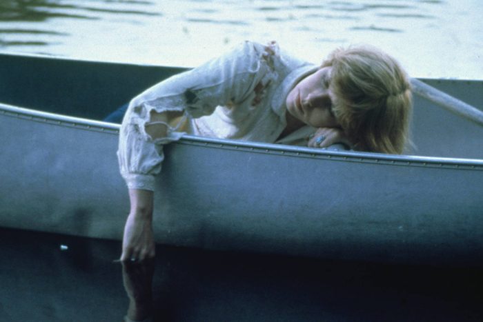 Person resting with arm hanging over a canoe's side, on a calm lake, wearing a distressed, long-sleeved shirt.