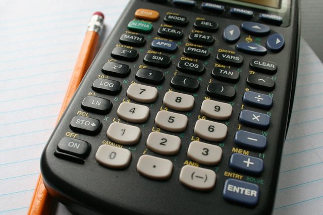 Calculator resting on lined paper, accompanied by a pencil, on a dark surface.