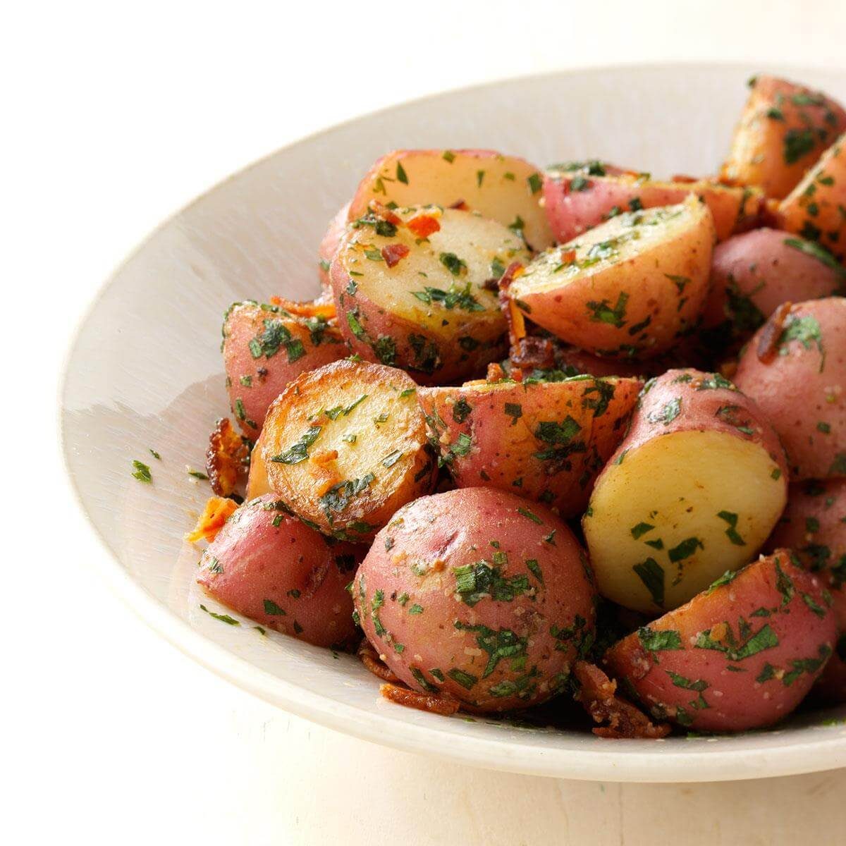 Potato pieces are garnished with herbs and spices, sitting in a white bowl, suggesting a freshly prepared dish.