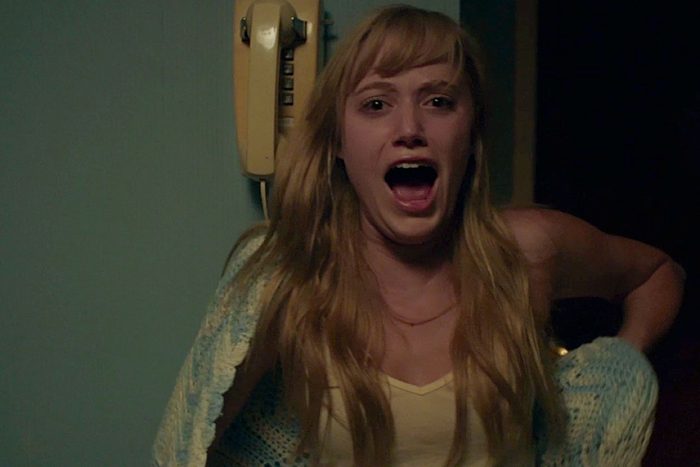 Woman screaming, hand held behind back, in a dimly lit room with a wall-mounted rotary phone.