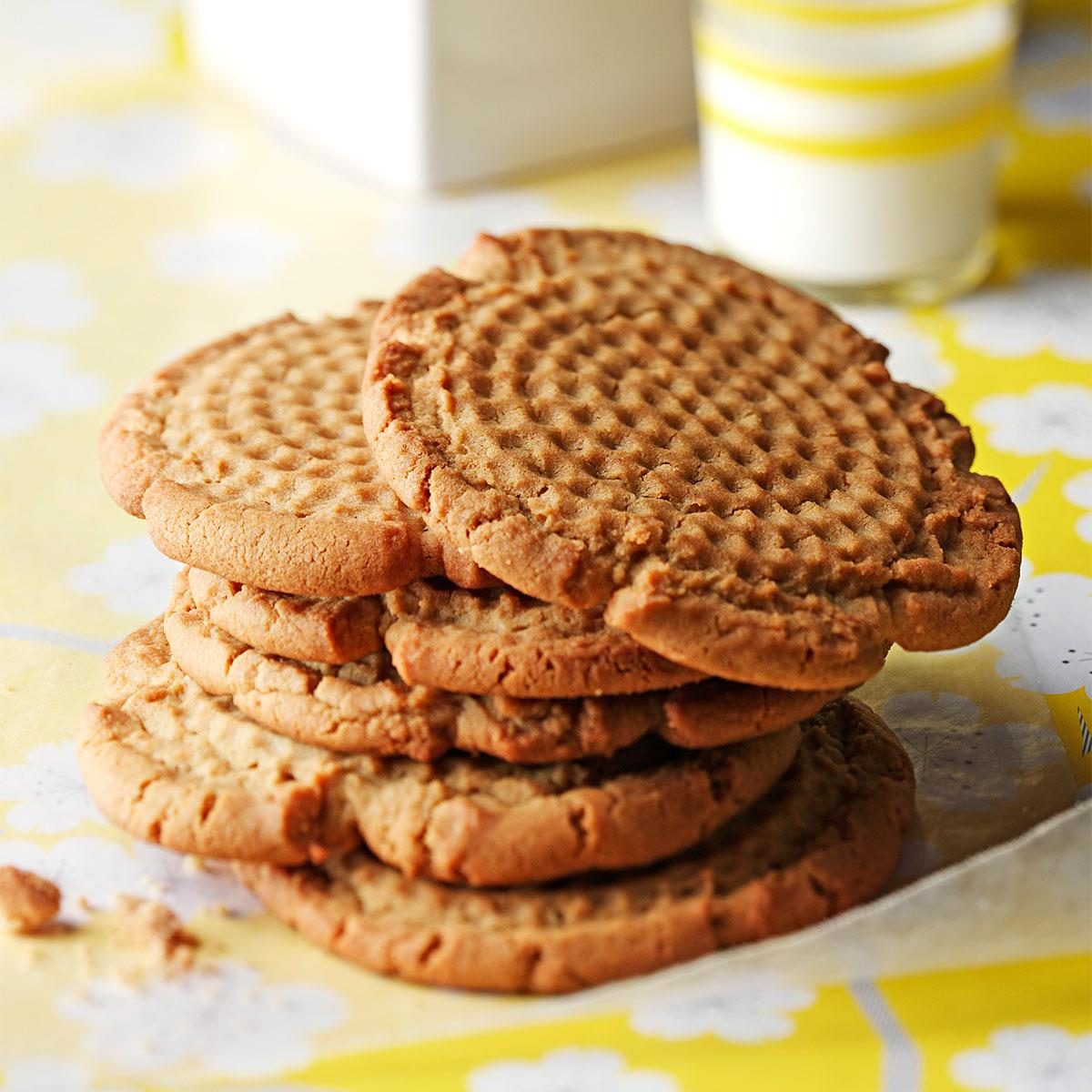 Cookies stacked neatly on a bright yellow tablecloth, with a glass of milk in the background.